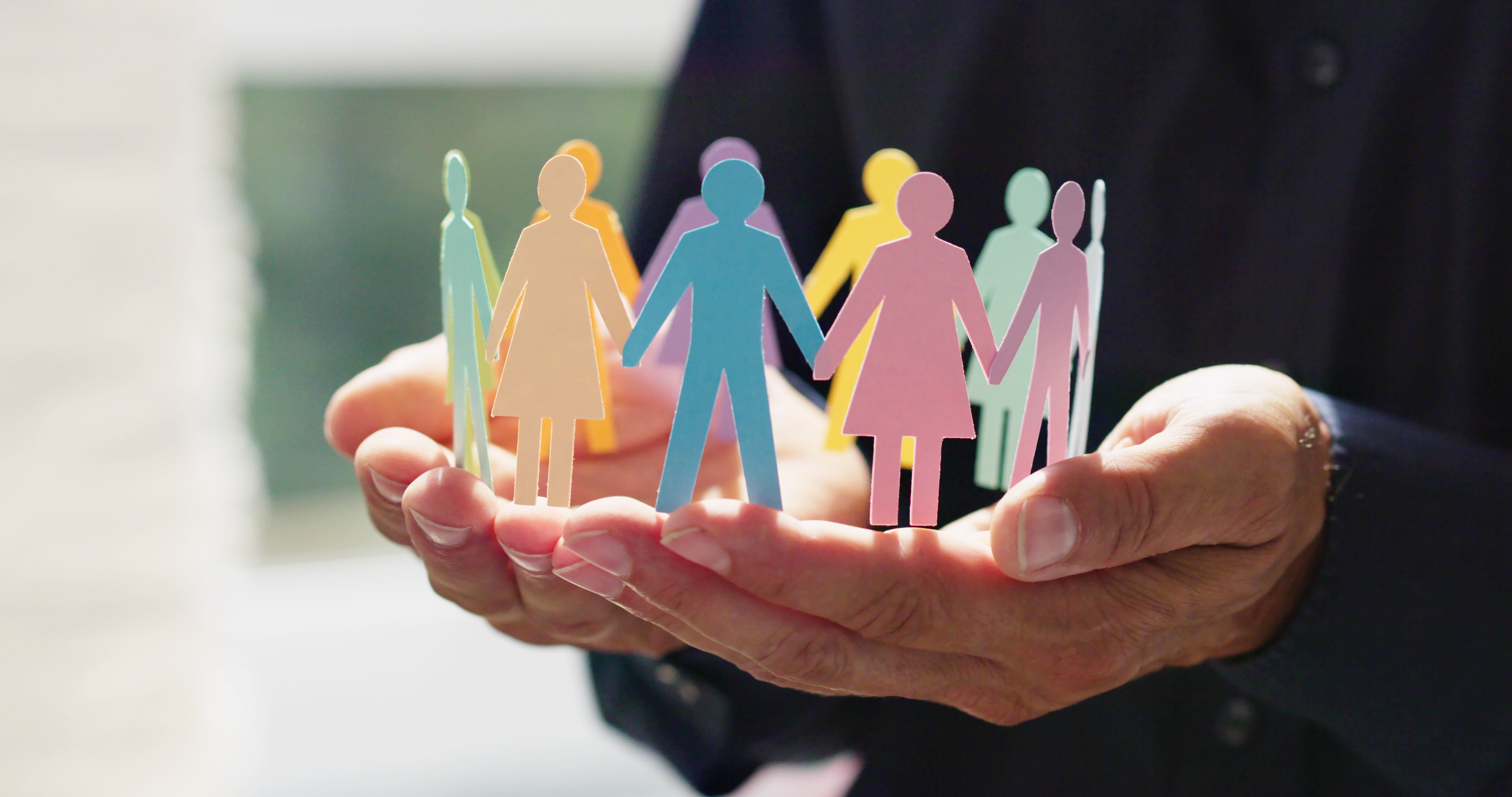Två händer håller upp en cirkel, formad av pappersfigurer i olika glada färger.
