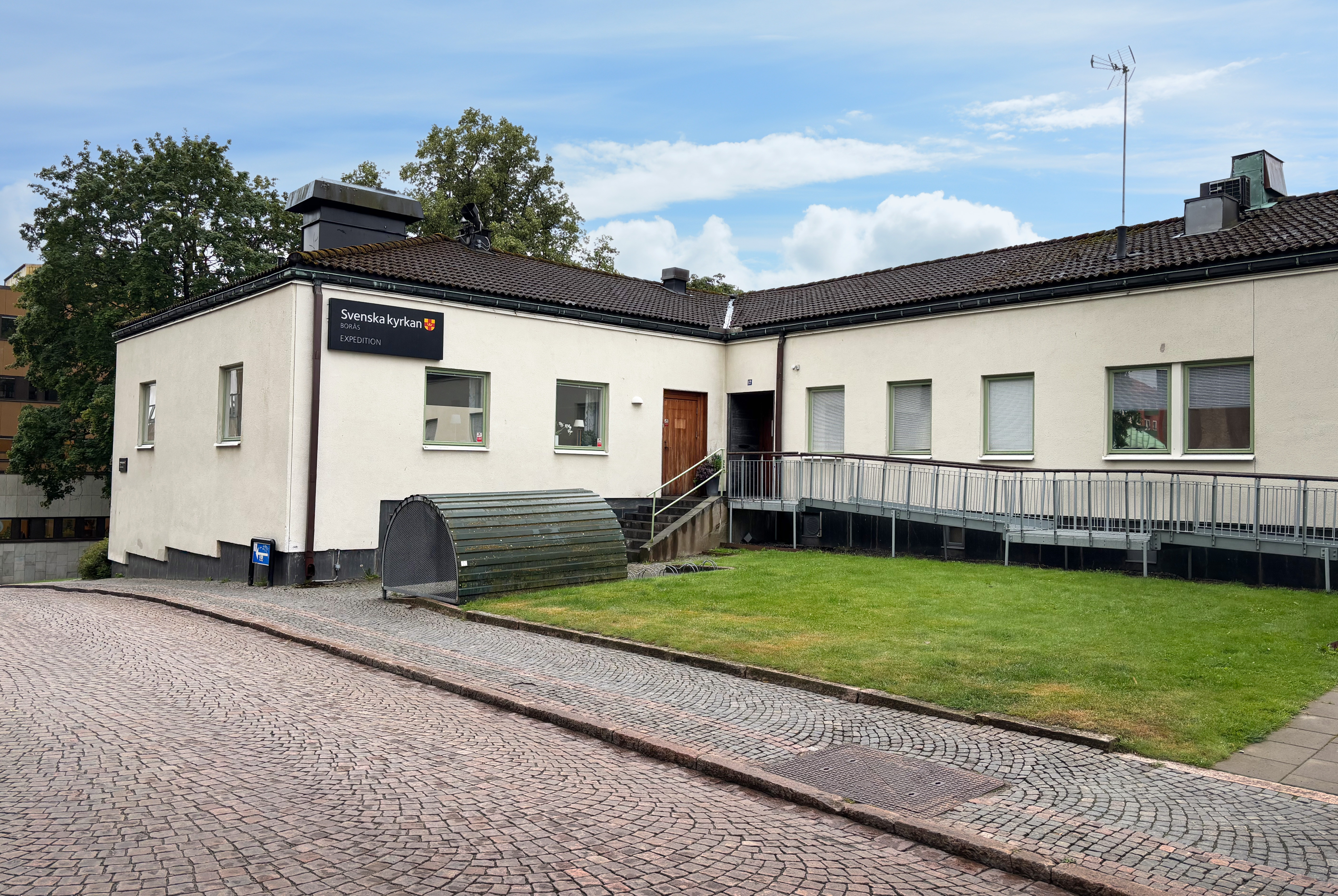 Ljus byggnad med stenlagd gata i förgrunden.