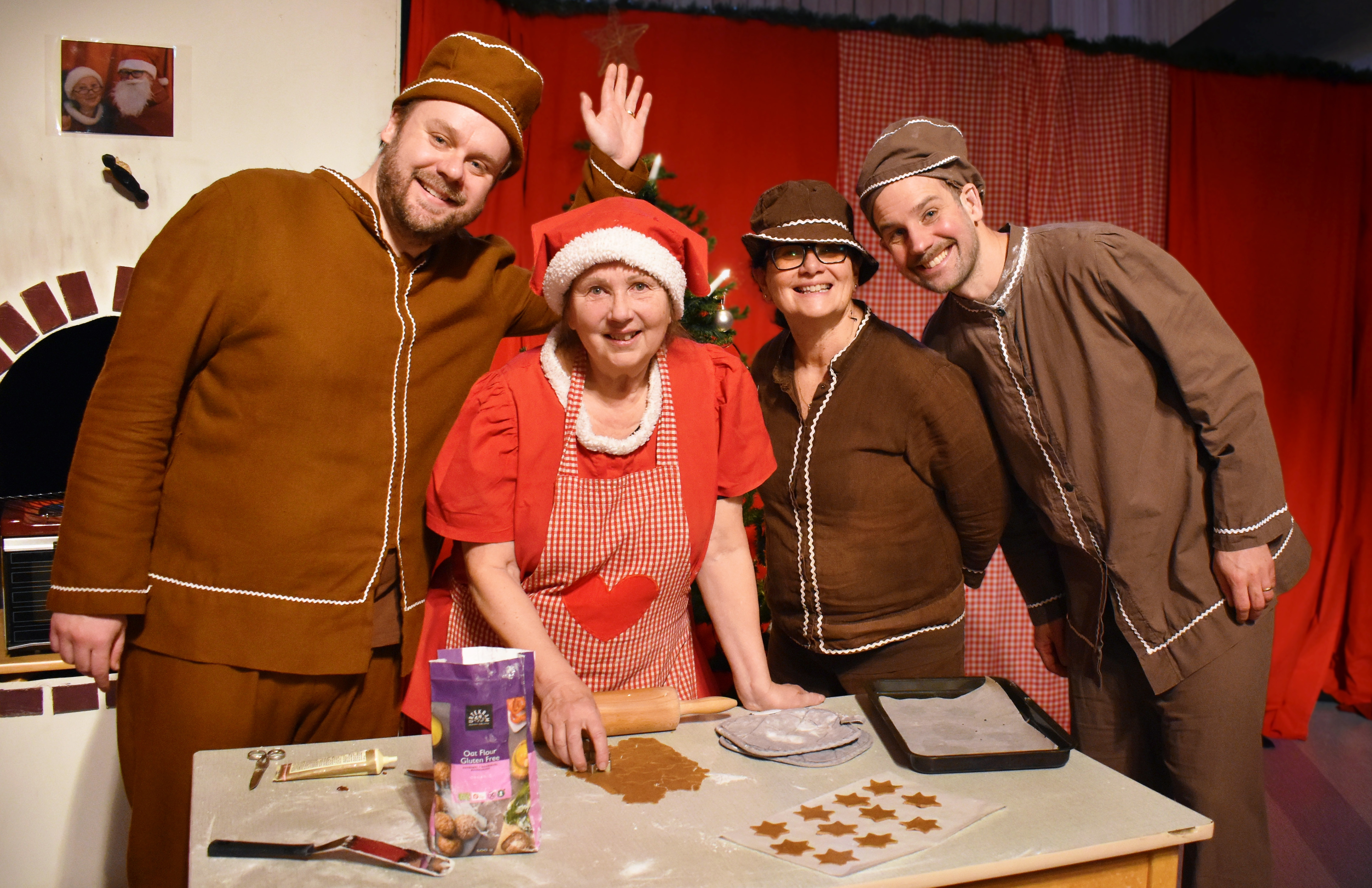 Scen med tomtemor och pepparkaksfigurer i teaterkök med julgran.