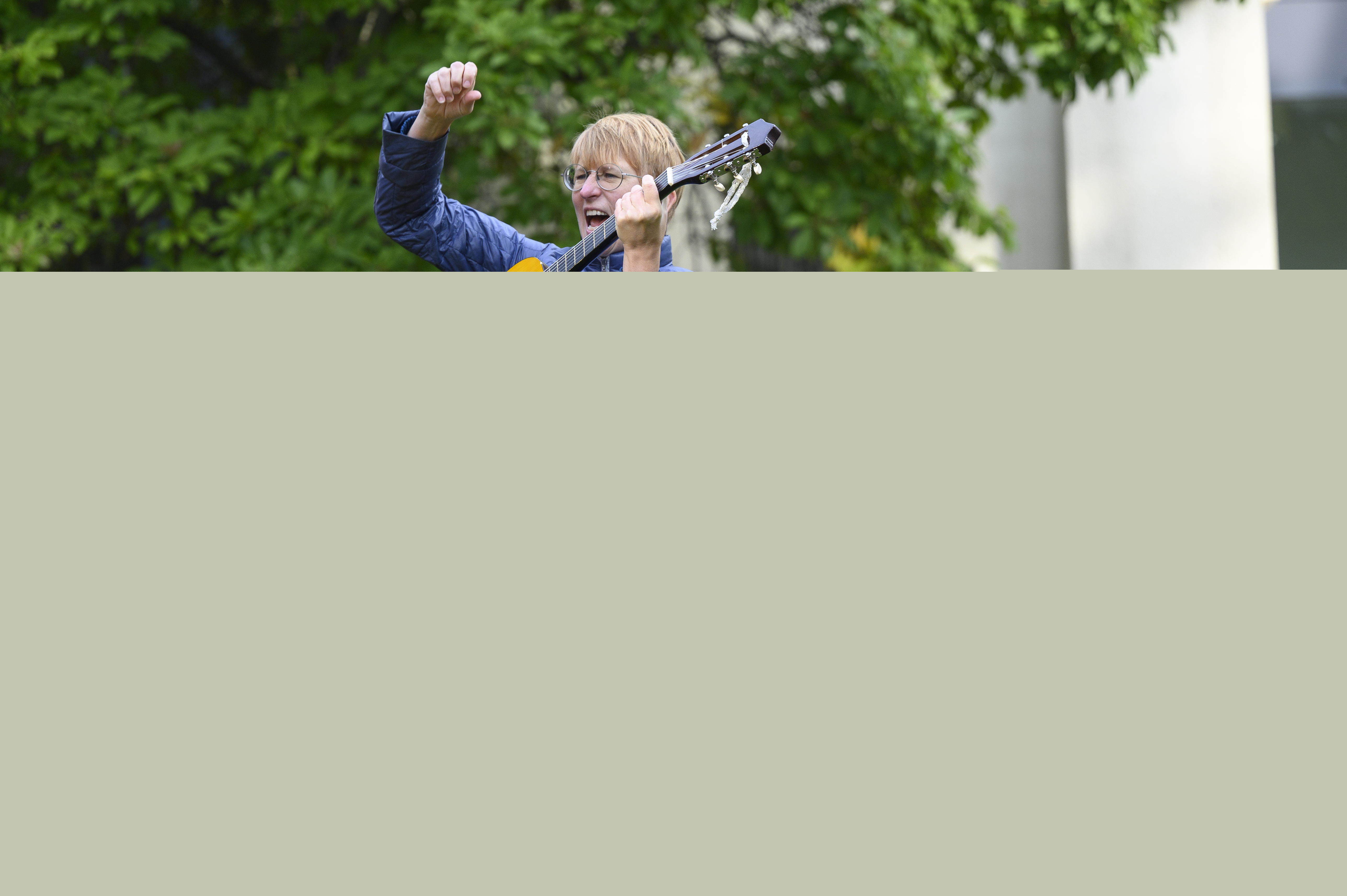 En kvinna står utomhus och spelar gitarr för en grupp barn.